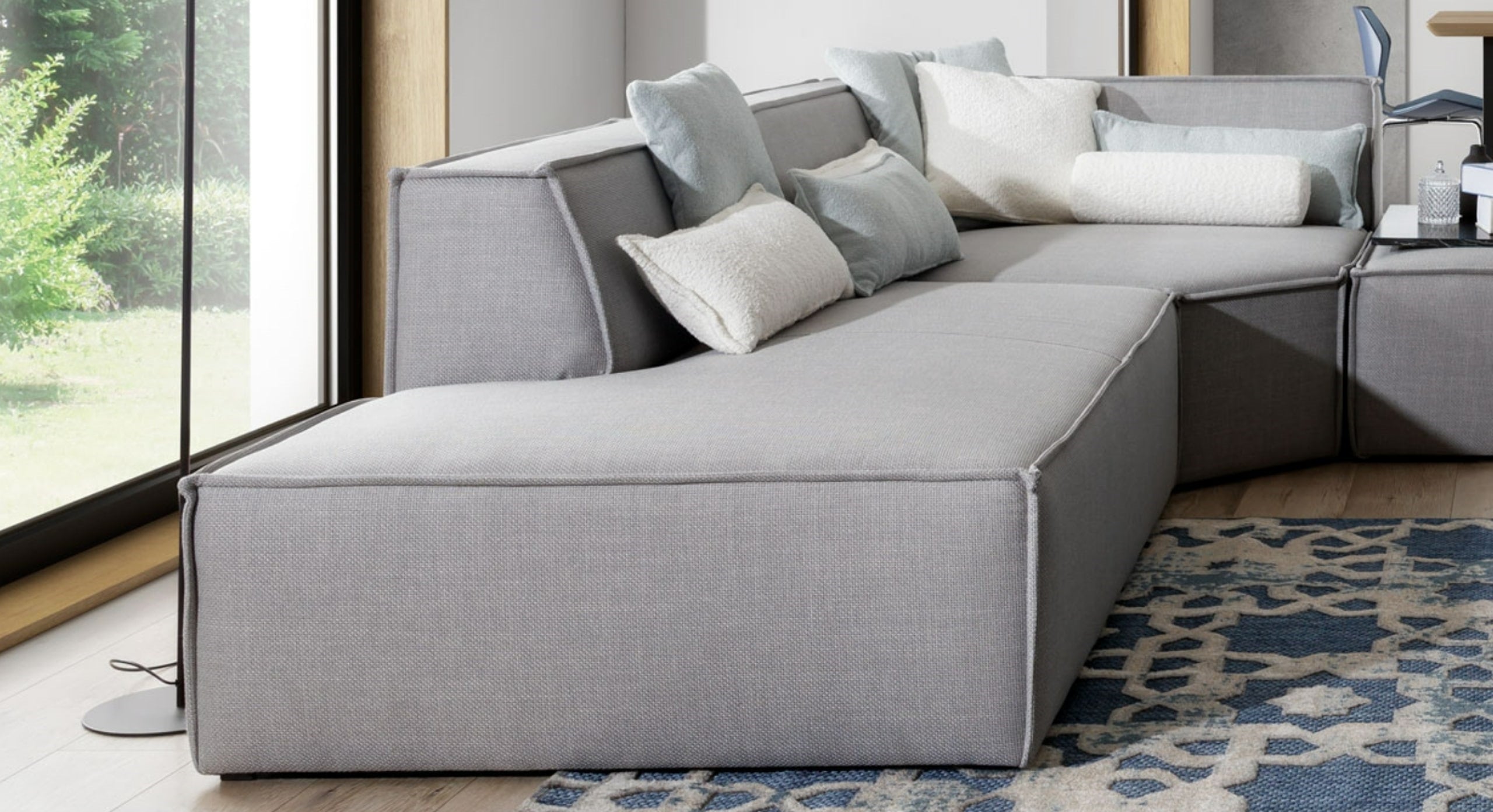 Close-up van het loungegedeelte van de hoekbank Sense, voorzien van verschillende zachte kussens in wit en lichtblauw voor extra comfort.