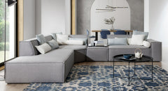 Grote hoekbank Sense met een moderne uitstraling, ingericht met kussens in zachte witte en blauwe tinten. De bank staat op een blauw-wit patroonkleed en wordt vergezeld door een ronde, zwarte salontafel met minimalistisch design.