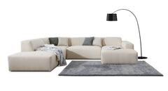 U-bank Vibe met chaise longue rechts, gestyled met een grijs vloerkleed, sierkussens en een plaid, gecombineerd met een zwarte booglamp. Deze opstelling creëert een warme, moderne sfeer die geschikt is voor eigentijdse woonkamers.