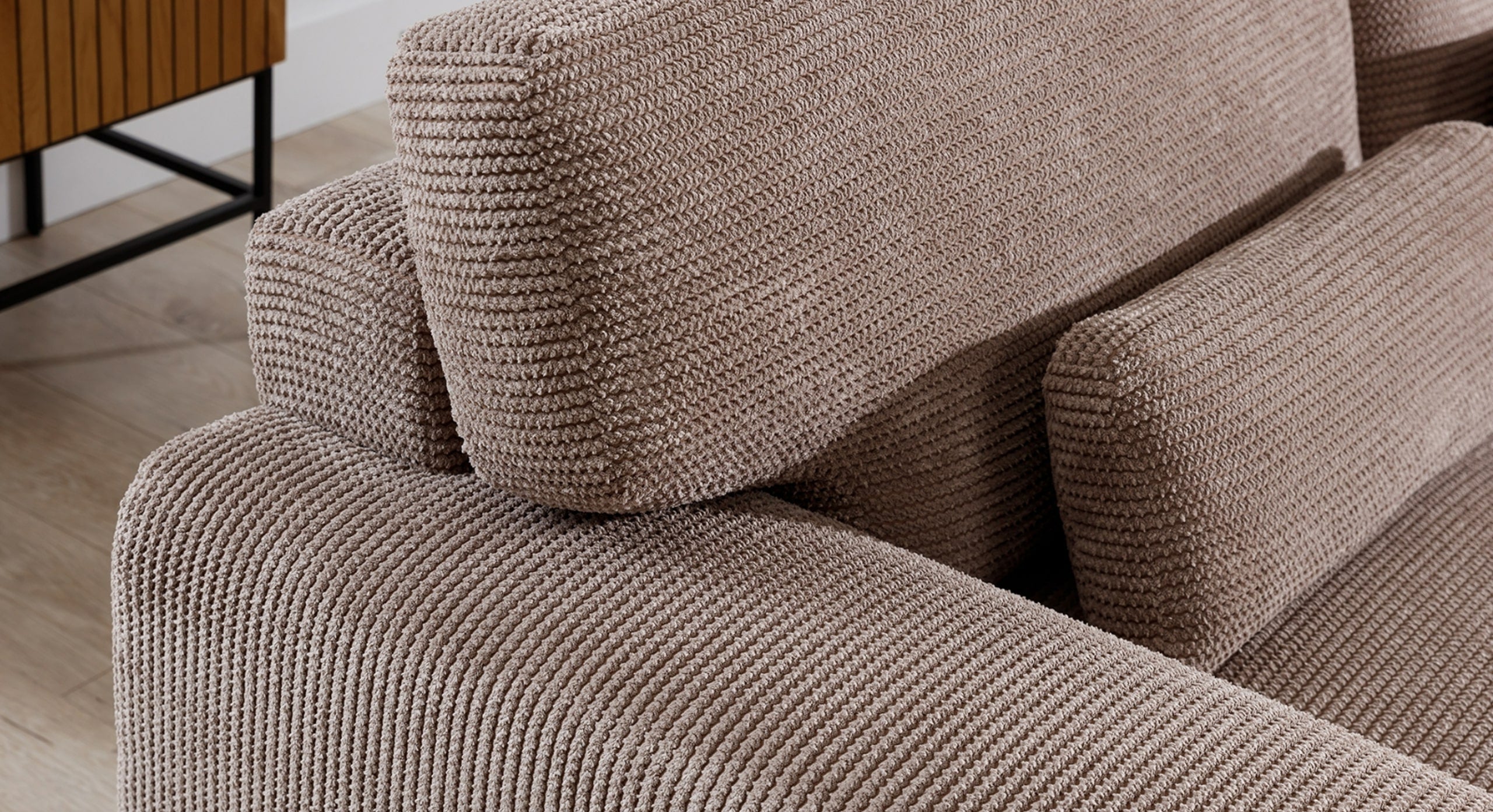 Close-up van de rugleuning en kussens van de beige hoekbank Fun. De kussens zijn royaal gevuld en gestoffeerd in een dikke ribfluwelen stof, wat een uitnodigend comfort en een moderne, warme uitstraling geeft.