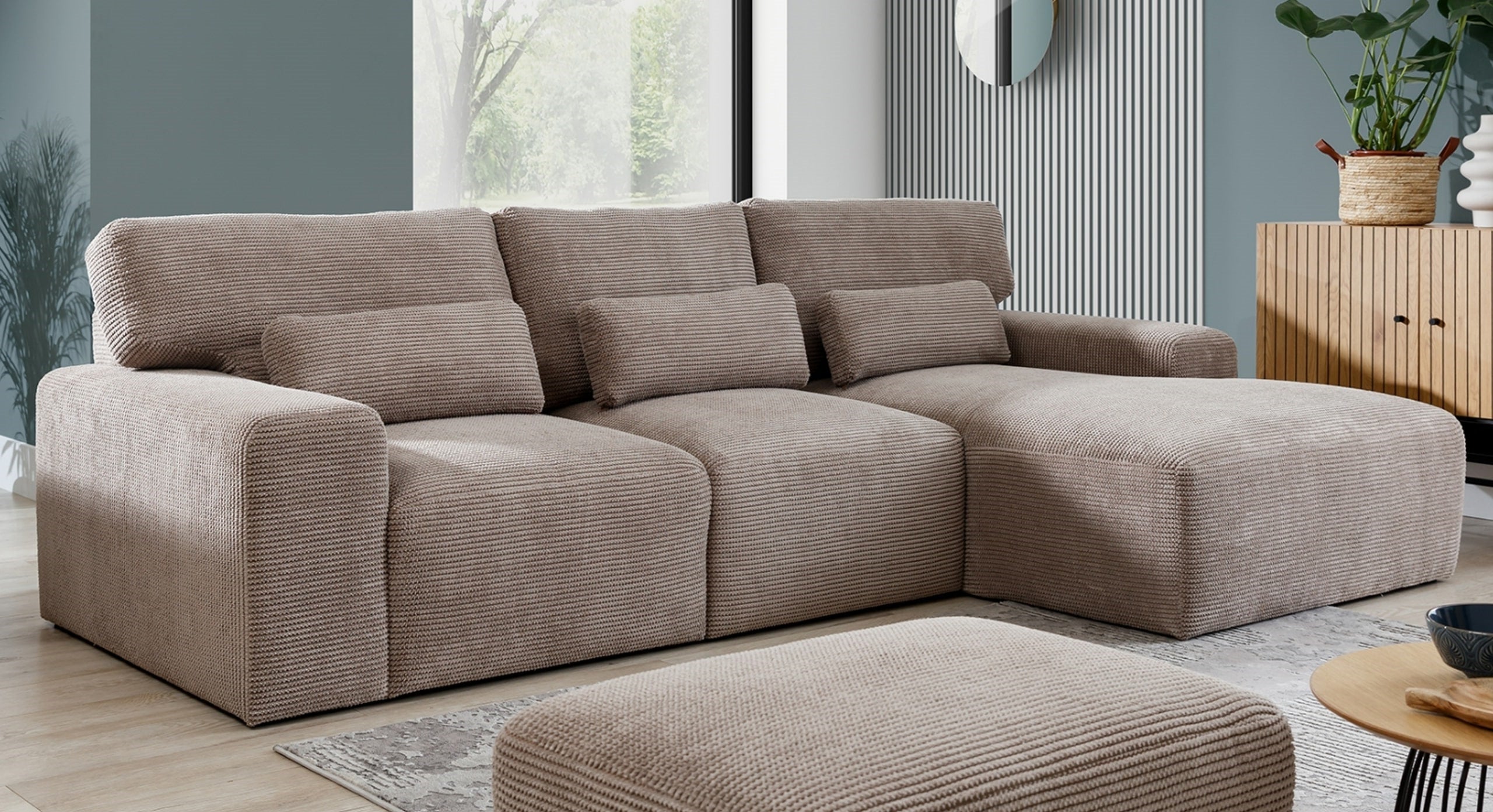 Hoekbank Fun met chaise longue rechts in een stijlvolle woonkamer, met een beige, geribbeld stofpatroon dat comfort en elegantie uitstraalt. De bank is voorzien van losse kussens en wordt gecombineerd met een bijpassende poef en houten accentmeubels, wat de ruimte een warme sfeer geeft.