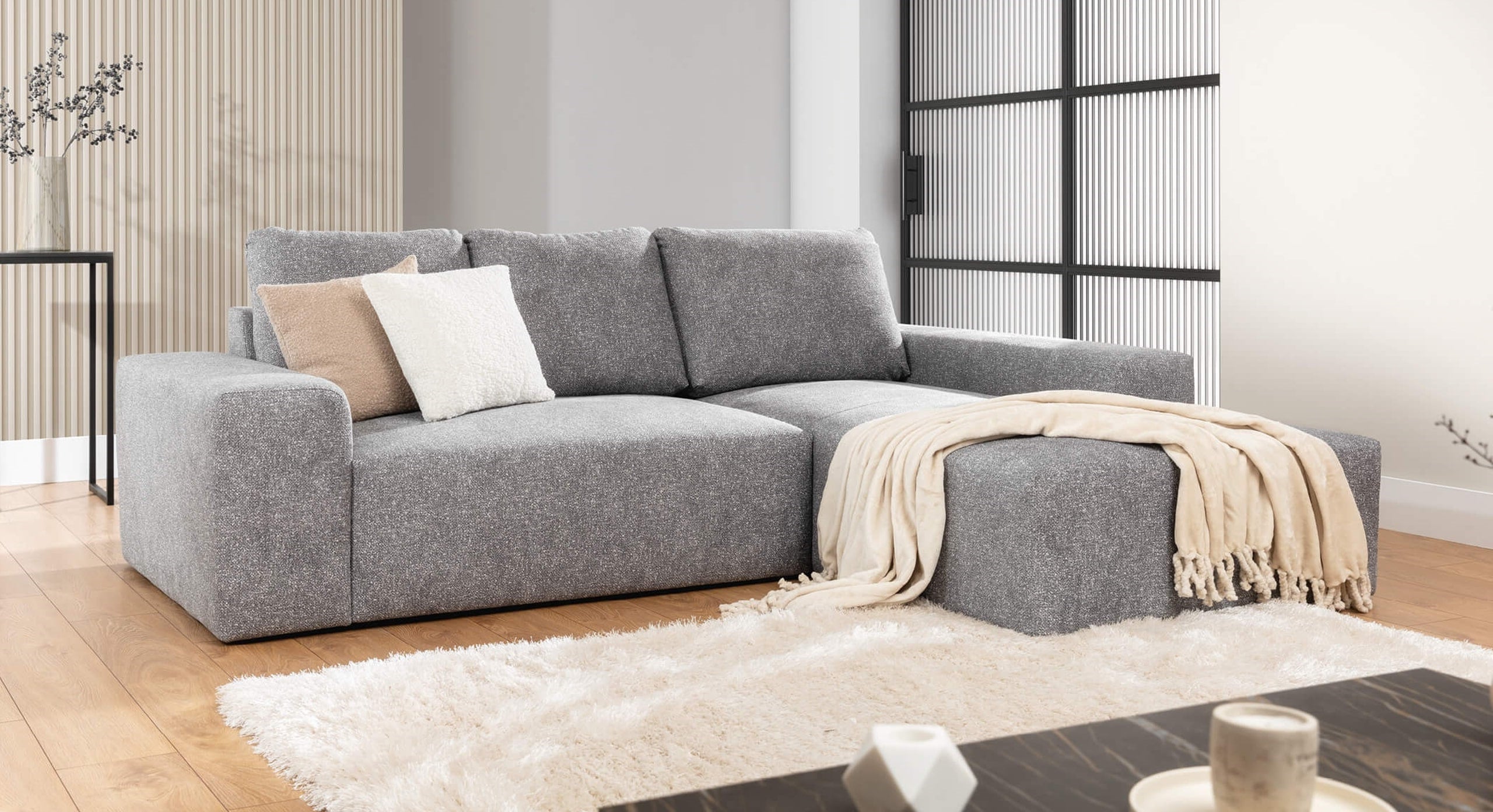 De Hoekbank Cosy Met Chaise Longue Rechts in een modern ingerichte woonkamer, voorzien van lichte kussens en een beige plaid, geplaatst op een zacht vloerkleed voor een warme en uitnodigende sfeer.