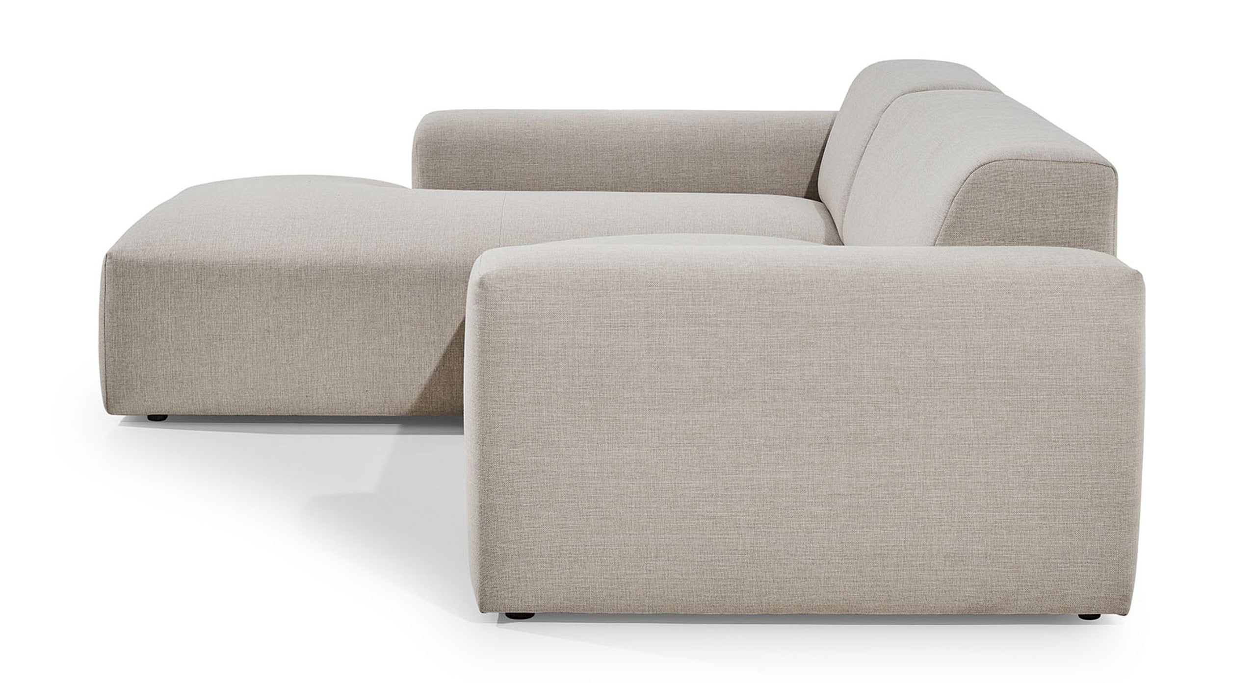 Zijaanzicht van de Hoekbank Vibe met chaise longue links, uitgevoerd in een neutrale beige stof. De bank heeft een strak en modern ontwerp met brede armleuningen en een diepe zitting, wat zorgt voor een eigentijdse en comfortabele uitstraling in de woonkamer.