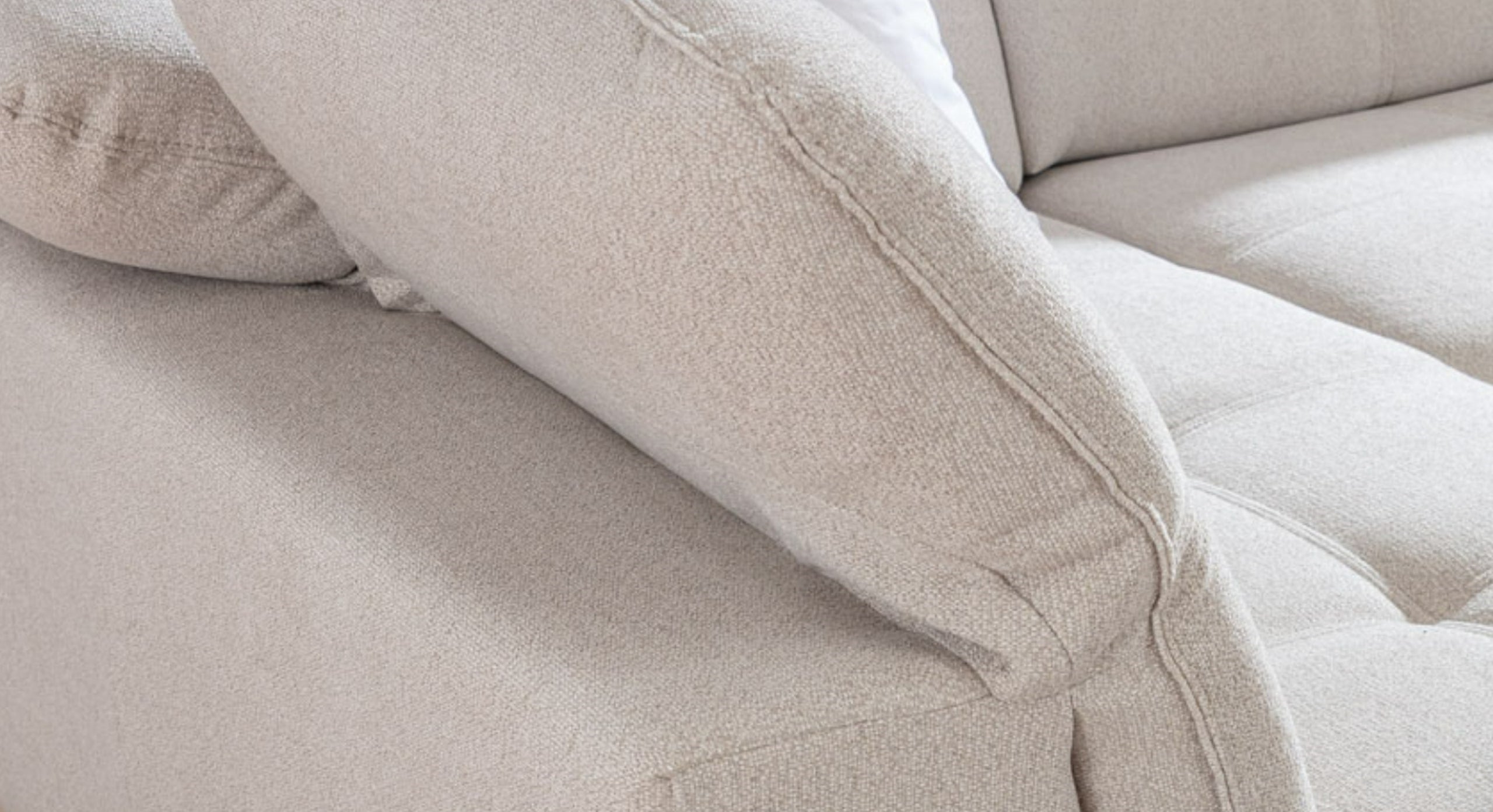 Close-up van de rugleuning en zitkussen van de U-bank Charm, in een lichte beige stof. De fijne details en stiksels geven de bank een luxe en comfortabele uitstraling, die perfect past in een modern en stijlvol interieur.