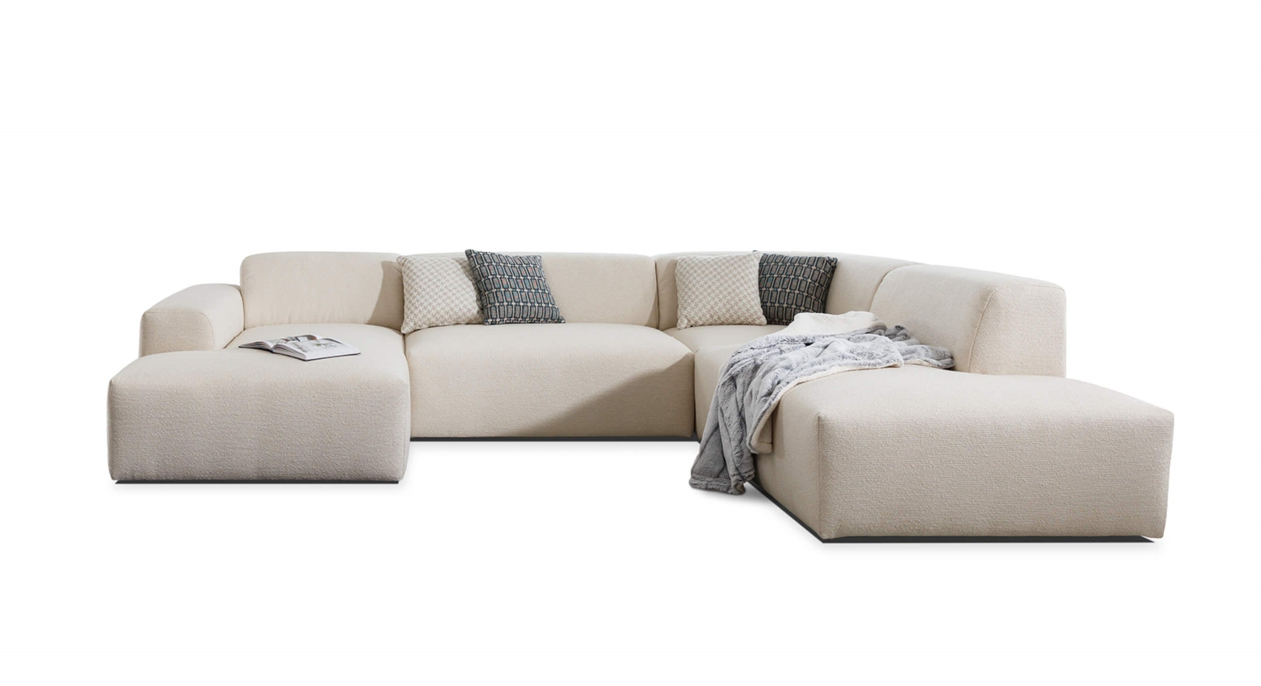 U-bank Vibe met chaise longue links, uitgevoerd in een lichte, neutrale bekleding en gedecoreerd met contrasterende kussens en een zachte plaid. Deze stijlvolle bank biedt een comfortabele en uitnodigende uitstraling voor moderne woonkamers.